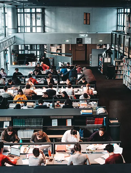 Ludzie siedzący w bibliotece, czytający książki i przeglądający regały z książkami.